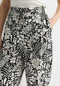 Mustat ja valkoiset kukkakuosiset housut, joissa on elastinen vyötärö, nyörityksellä ja sivutaskuilla rentoa istuvuutta varten.