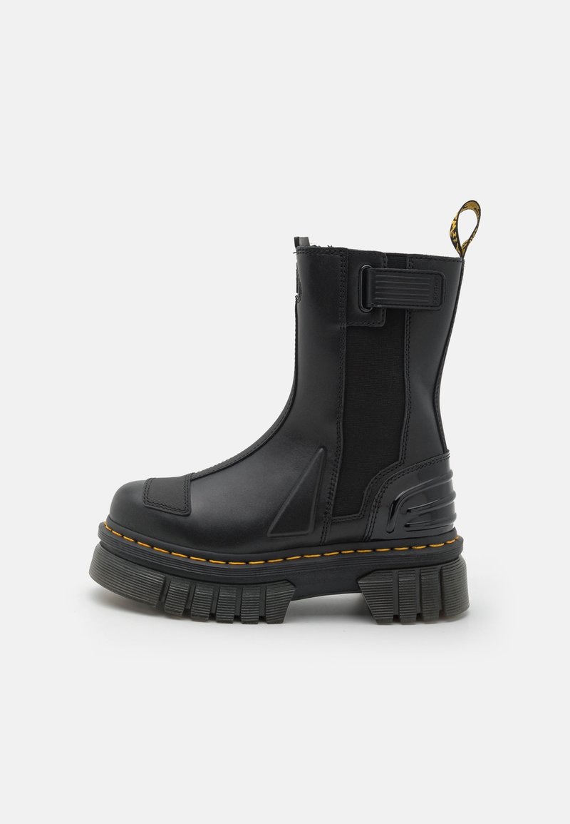 Botte plateforme noire à semelle épaisse crantée, couture jaune, panneau élastique latéral et languette de traction à l'arrière sur fond blanc.
