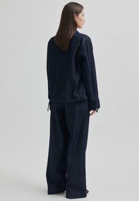 Jachetă din denim închis și pantaloni largi cu un finisaj texturat. Jacheta are o croială lejeră și manșete ajustabile.