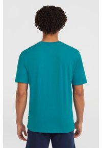 Camiseta de manga corta en color teal, fabricada en algodón suave, cuenta con un cuello redondo y un corte relajado, con costuras visibles a lo largo de las costuras.