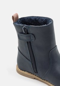 Marineblaue Leder-Stiefelette mit seitlichem Reißverschluss, blauen Nähten, fellgefüttert, glitzerndem pinkem Ziehband und braunem Gummisohle.