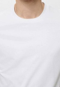 Gros plan sur une personne portant un t-shirt blanc à col rond, montrant la zone du cou et du haut de la poitrine.