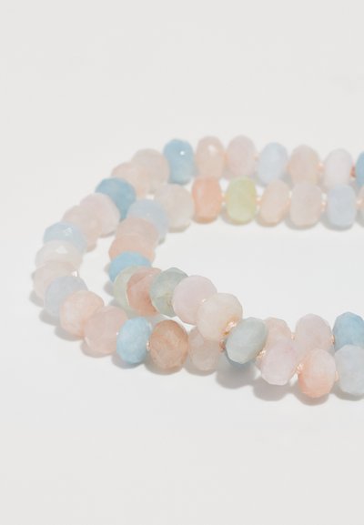 Náhrdelník s korálkami vyrobený z mnohostranných pastelových kameňov vrátane ružovej, modrej a zelenej, navlečený na tenkom drôte s kovovými akcentmi.