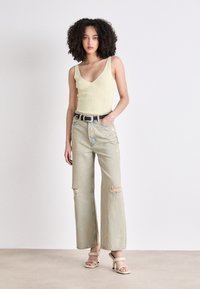 Light yellow ribbed tank top paired with light blue wide-leg jeans featuring distressed details. Black belt and light-colored heeled sandals.