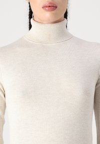Pulover bej cu guler înalt, realizat dintr-un material tricotat moale și ușor, având un guler cu textura ribbed și o textură uniformă și netedă.