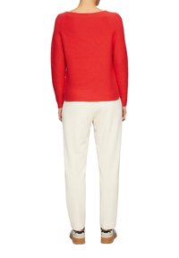 Rode gebreide trui met een ronde hals, gecombineerd met crèmekleurige tapered pants en casual sneakers, gezien vanaf de achterkant.