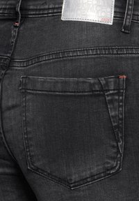 Svarta jeans i denim med en bakficka, sömnadsdetaljer och ett märke. Materialet har en något texturerad yta.