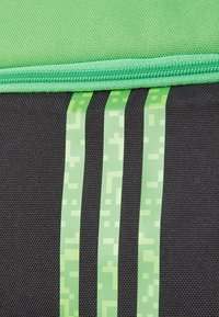 Un tessuto nero con tre strisce verticali pixelate verdi. La parte superiore è di un verde più chiaro con una superficie texture e una cerniera.