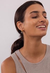 Gold- und Silberohrringe in Form von Creolen mit strukturiertem Design, polierter Oberfläche und ineinandergreifenden Ringen. Getragen von einem Model.