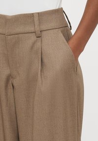 Brūnas pielāgotas bikses no teksturētas auduma, ar sānu kabatām, vidēja augstuma jostasvietu un klasisku taisnu kāju dizainu.