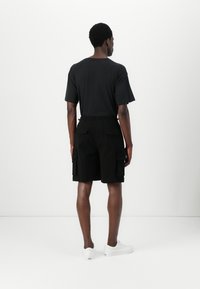 Sort t-shirt med korte ærmer kombineret med sorte cargo-shorts med flere lommer. Hvide sneakers fuldender outfittet.
