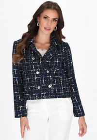 Jachetă din tweed bleumarin cu un model texturat de pătrate albe, albastre și galbene; design cu două rânduri de nasturi, cu nasturi metalici și guler cu colțuri.