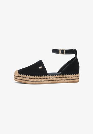 Espadrille noire à talon compensé avec bride à la cheville, boucle dorée et détail de semelle en jute tressé, vue latérale sur fond blanc.