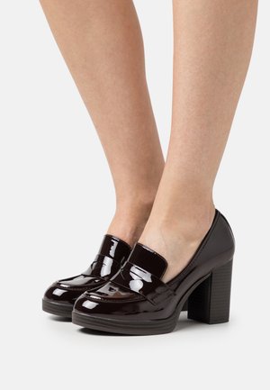 Escarpins en vernis noir avec un bout rond, présentant un design surélevé à l'avant et un talon block texturé.