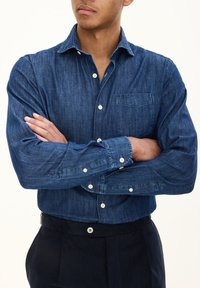 Donkerdenim button-up shirt met een kraag, lange mouwen en een borstzak. Voorzien van witte knopen en een textuurafwerking.