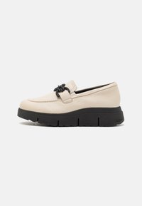 Béžová kožená slip-on obuv s černou gumovou podrážkou, s vyvýšeným podpatkem a dekoračním černým kováním na nártu.
