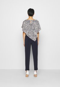 T-shirt ample à manches courtes avec un motif abstrait bleu marine et blanc, associé à un pantalon sombre et des chaussures à talons blancs. Détail en forme de clé au dos.