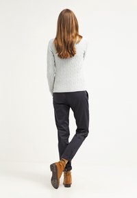 Maglione grigio chiaro a treccia, pantaloni blu scuro e stivali alla caviglia marroni. Il maglione presenta un motivo testurizzato, mentre i pantaloni hanno una vestibilità comoda.
