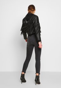 Czarna skórzana krótka kurtka z frędzlami, zestawiona z ciemnymi jeansami z wysokim stanem i botkami o błyszczącym wykończeniu.