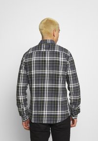 Kariertes Hemd in Grautönen, Grün und Weiß, mit einem Button-down-Kragen, langen Ärmeln und einem abgerundeten Saum.