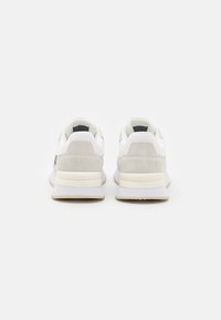 Białe i jasnoszare buty sportowe z zamszowymi akcentami, wyściełaną podeszwą i małym wytłoczonym logo na śródpodeszwie. Widok z tyłu z zaokrąglonymi piętami.