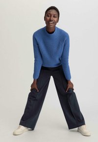 Pull en tricot côtelé bleu avec un col rond, associé à un pantalon large noir et des baskets blanches. Textures douces et design décontracté.