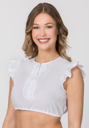 Junge Frau lächelnd, trägt eine weiße kurz geschnittene Bluse mit gerafften Kapuzenärmeln und einem strukturierten Vorderteil.
