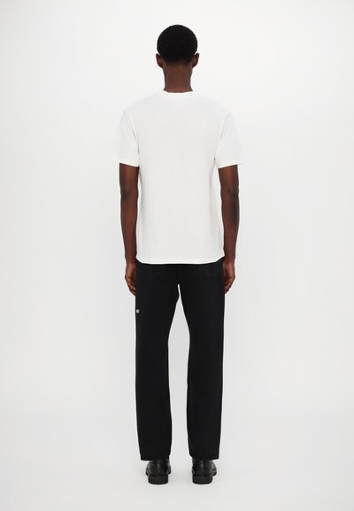 White cotton t-shirt with short sleeves and round neckline, paired with black, relaxed-fit trousers, featuring subtle detailing.