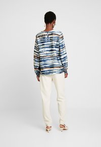 Långärmad blus i blåa och neutrala ränder, med rundad halsringning och knappstängning bak, matchad med ljusa byxor.