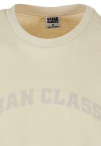 Világos krémszínű, pamut póló lekerekített nyakkivágással. "URBAN CLASSICS" felirat homorú szürke betűkkel a mellkasán. Simogató tapintású. M-es méret.