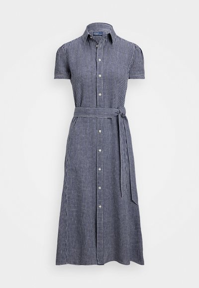 Kratso piedurkņu pogājams kleita tumši ziltā un baltā šaha rakstā, ar pievilktu jostasvietu un atbilstošu jostu, izgatavota no gaisīga auduma.