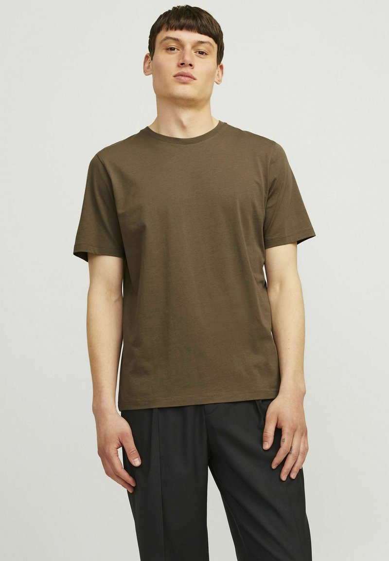 Brown cotton t-shirt with a crew neck, short sleeves, and a relaxed fit, worn with dark pants. Smooth texture, simple design.