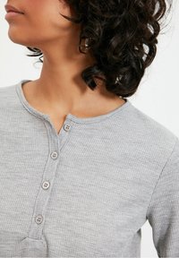 Grå ribbad långärmad topp med rund halsringning och femknapps knappslå fram. Materialet verkar mjukt med en strukturerad yta.