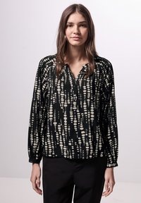 Blusa nera con motivo a pois bianchi allungati, maniche lunghe, apertura con bottoni e polsini elasticizzati; texture del tessuto liscia.