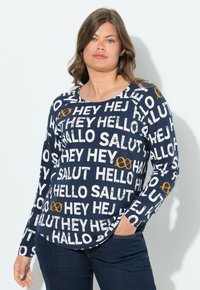 Námořnická košile s dlouhým rukávem s výrazným bílým textem, který obsahuje pozdravy v několika jazycích a oranžovým akcentovým symbolem. Měkká tkanina.