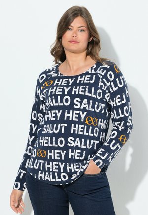 Marineblauwe shirt met lange mouwen, gekenmerkt door een gedurfde witte tekstpatroon met begroetingen in meerdere talen en een oranje accent symbool. Zacht materiaal.