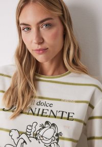 Witte fleece sweatshirt met groene strepen; heeft een Garfield graphic en de tekst "il dolce far niente," met "ENJOYING" geborduurd in roze.