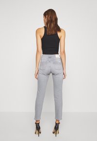 Šedé úzké džíny s středním pasem, které mají klasický pětikapsový design a jemné opotřebení na lemech. V kombinaci s černými podpatky.