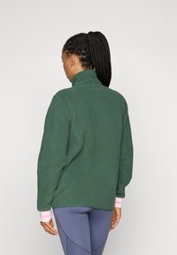 Grønn fleece genser med høy krage, lange ermer og rosa stripete mansjetter. Myk tekstur og avslappet passform. Bakside vist.