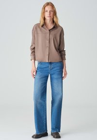 Brown button-up shirt with a collar, paired with light blue wide-leg jeans. The shirt has a smooth texture and relaxed fit.