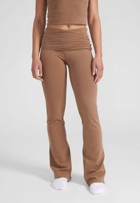 Bruine flare leggings gemaakt van zacht, rekbaar materiaal met een gerimpelde tailleband en een gladde textuur, gecombineerd met witte sokken.
