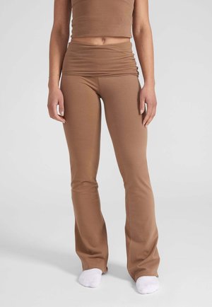 Leggings marroni a zampa d'elefante realizzati in materiale morbido e elasticizzato, con una vita arricciata e una superficie liscia, abbinati a calzini bianchi.