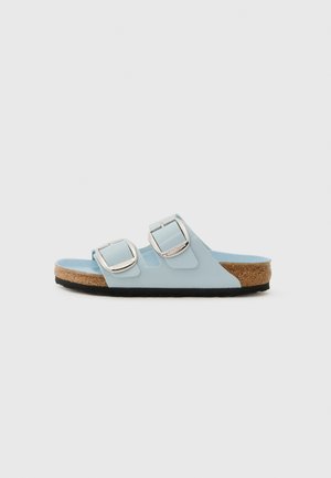 Light blue slide sandal with two adjustable silver buckles, cork footbed, textured black outsole, and smooth upper material.