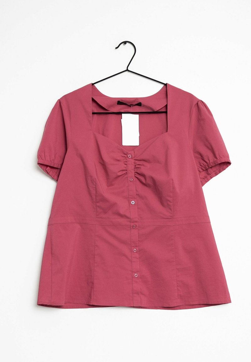 Blouse rose poudrée à manches courtes avec boutons sur le devant et détail froncé sur la poitrine, suspendue sur un cintre noir sur fond blanc.