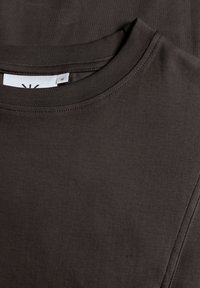 Dunkelgraues Baumwoll-T-Shirt mit Rundhalsausschnitt, das eine glatte Textur aufweist und ein Etikett mit der Größe M im Innenbereich des Ausschnitts hat.