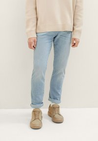 Jeans de culoare albastră deschisă, cu o croială slim, cu manșete răsucite, asociați cu adidași bej cu sistem de șireturi și material texturat.