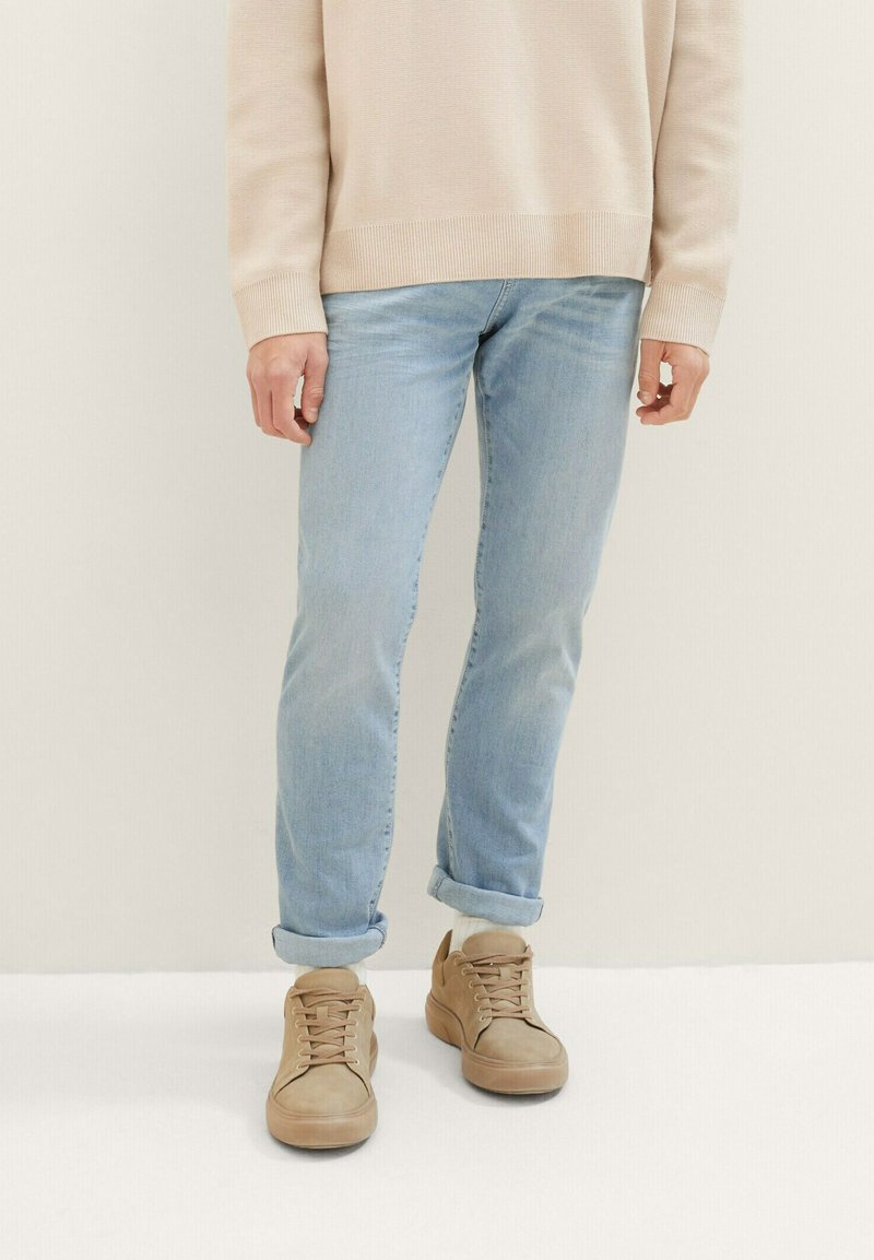 Jeans de culoare albastră deschisă, cu o croială slim, cu manșete răsucite, asociați cu adidași bej cu sistem de șireturi și material texturat.