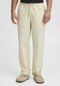 Lys beige elastiske bukser med en snøre i taljen. Glat tekstur og vidde ben-design, med sidelommer og subtil syning.