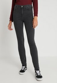 Jeans skinny negros de cintura alta, fabricados en denim con un ligero estiramiento, detalles deslavados y costuras mínimas. Combinados con zapatillas negras y blancas.