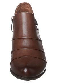 Chaussure en cuir marron avec des plis horizontaux, bout arrondi et détail de boucle sur le côté. Texture lisse et léger éclat à la surface.